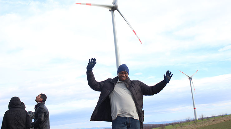 young African stands under windmills and waves into the camera